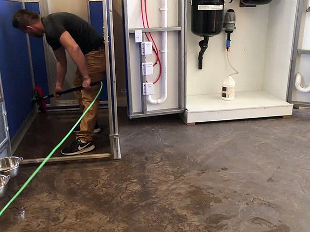 Staff member cleaning a kennel run floor using a hose plugged into a wall-mounted Aqua-Air station